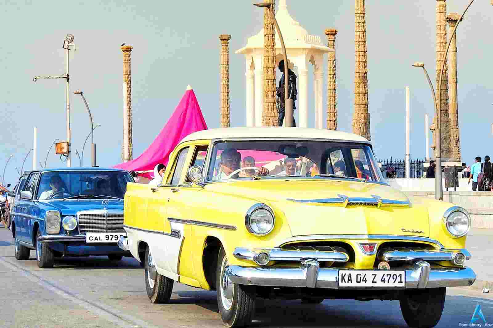 Rock beach with tall big Mahatma Gandhi statue. There is a long road with a yellow-blue car.